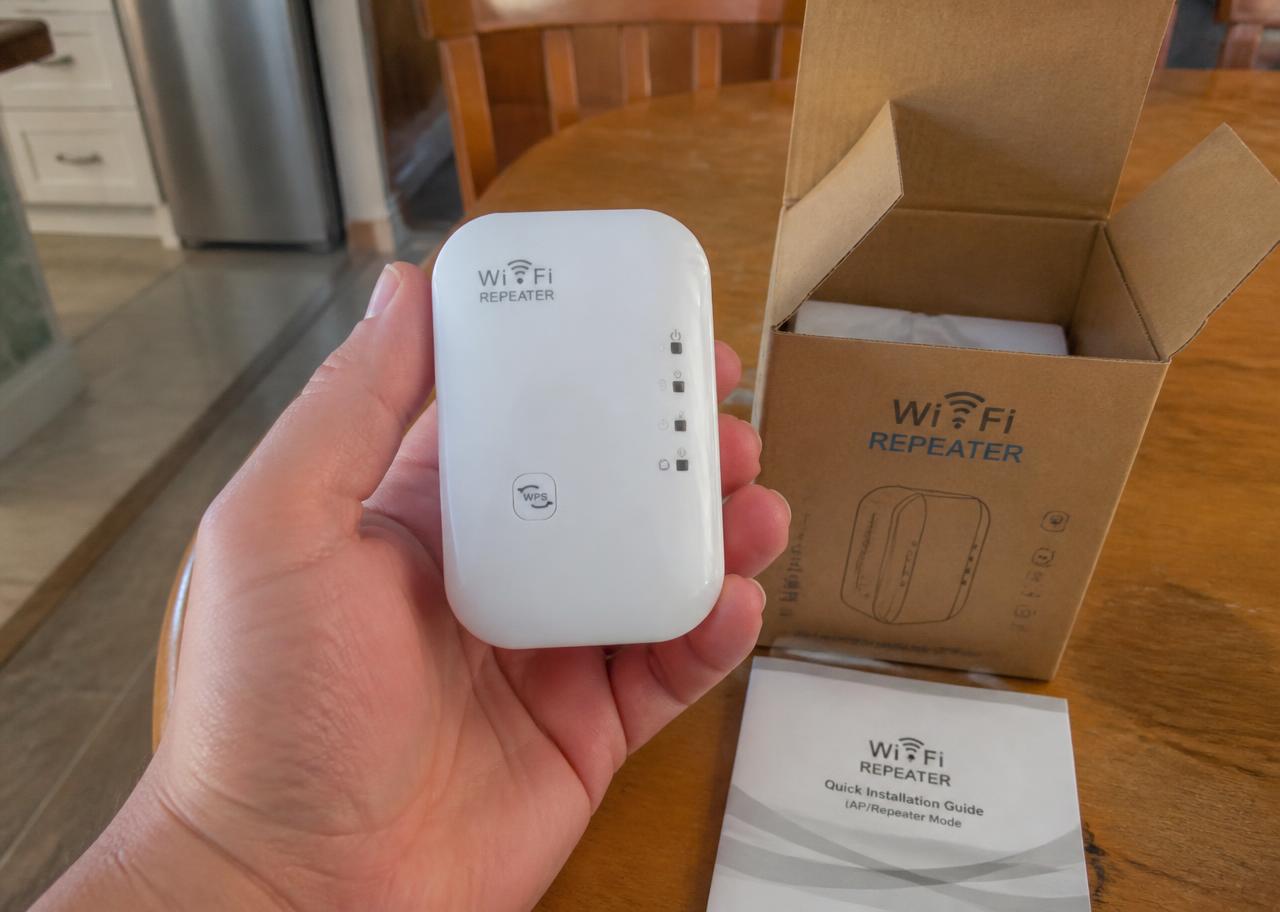Répéteur Wi-Fi UltraBoost tenu dans la main, à côté de sa boîte en carton